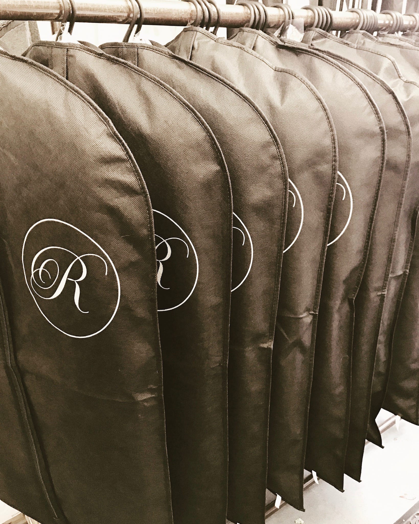 Row of black Reids reusable garment bags with R monograms